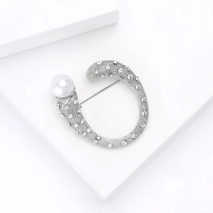 Dettaglio spilla argento a forma di C con pavé di cristalli e una grande perla bianca