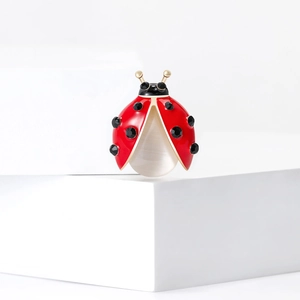 Red enamel ladybug brooch with white cat eye stone and golden metal on white stand
