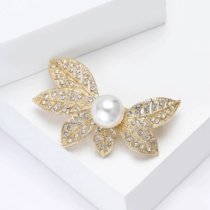 Détail macro d'une broche feuille dorée avec perle blanche et strass scintillants