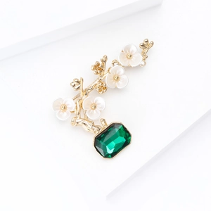 Macro detail of plum blossom brooch featuring emerald green gemstone and golden branches