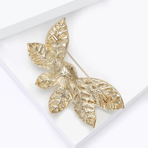 Vue détaillée d'une broche feuille dorée ajourée avec cristaux et épingle de sûreté