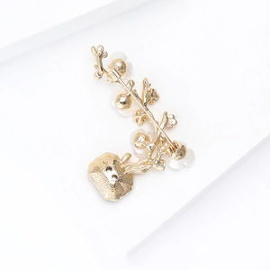 Detail view of the golden floral plum blossom brooch with safety pin and white pearls