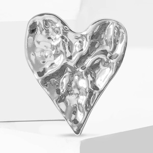 Broche cœur argentée texturée martelée sur support géométrique blanc moderne