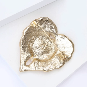 Detail of heart poppy brooch back with safety pin clasp on matte gold alloy surface
