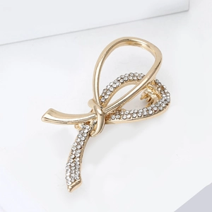 Detailed macro view of a gold-plated ribbon knot brooch featuring sparkling white rhinestones