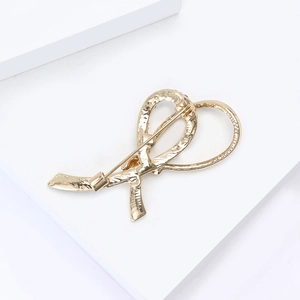 Detailed close-up of a golden ribbon knot brooch with elegant ripple textures and a pin back
