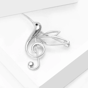Detailed close-up of a silver hummingbird and treble clef brooch on white background