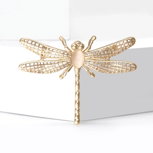 Elegant gold hollow dragonfly brooch with white cat-eye gemstone on white geometric steps