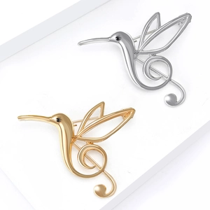 Elegant gold and silver hummingbird music note brooches on a white geometric display