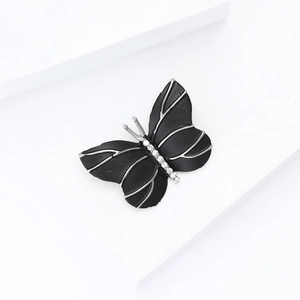 Élégante broche papillon argent et noir avec cristaux sur des socles blancs épurés