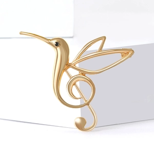 Detailed close-up of golden hummingbird brooch featuring a musical treble clef design