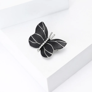 Élégante broche papillon noir et argent avec cristaux sur un socle blanc moderne
