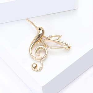 Detail view of a gold hummingbird and treble clef brooch with a polished finish