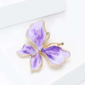Dettaglio di una spilla a farfalla in smalto viola con cristalli scintillanti su sfondo bianco