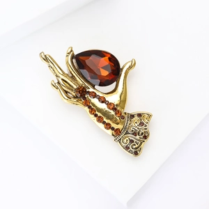 Detail of vintage hand-shaped brooch in gold finish with amber drop crystal and floral carving