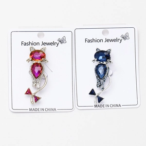Close-up of cat-shaped crystal brooches in pink-orange and blue on jewelry cards