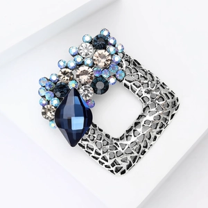 Macro shot of silver vintage square brooch with intricate grid patterns and blue crystals