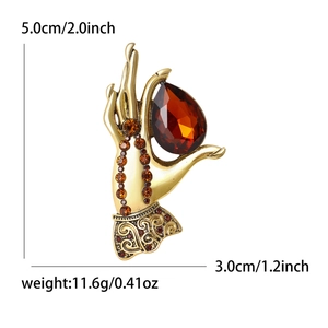 Elegant gold hand-shaped brooch holding a large pear-cut red gemstone with amber crystals