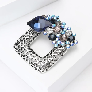 Close-up of geometric镂空 square brooch featuring a deep blue crystal and silver texture
