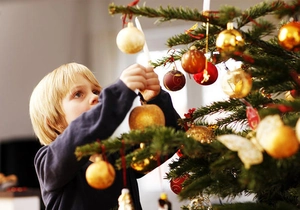 Festive mix of shiny and matte Christmas ornaments being hung on a tree by a boy