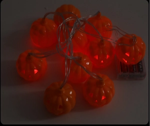Close-up of glowing hollow pumpkin LED string lights with a transparent battery box
