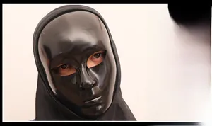 Detail of a black glossy full face mask with realistic facial features and fabric hood