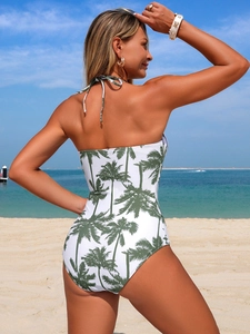 Detailed back view of a one-piece swimsuit with green palm tree print on a tropical beach