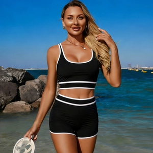 Bikini sportivo nero a due pezzi con finiture bianche a contrasto su sfondo spiaggia