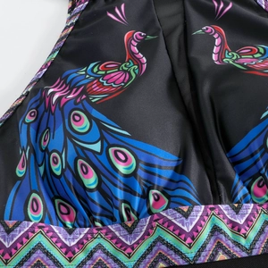 Detailed macro view of black swimwear fabric with vibrant peacock prints and geometric patterns