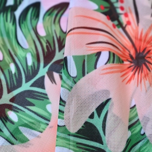 Close-up of mesh fabric featuring tropical green monstera leaves and orange floral prints