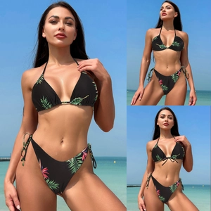 Detail of black bikini with tropical palm leaf and red floral patterns on the beach