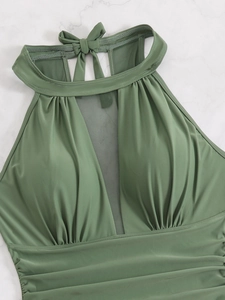 Detail of sage green halter swimsuit with mesh insert and side ruching on marble