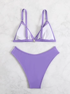 Flat lay of purple bikini set with white lining and metal clasp on marble surface
