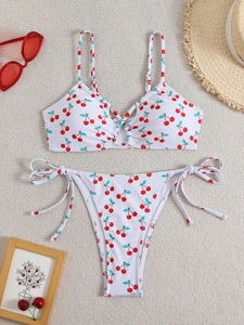Detailed flat lay of white two-piece bikini featuring red cherry prints and side-tie bottoms