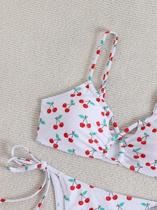 Detail of white bikini with red cherry print featuring lace-up sides and cutout top