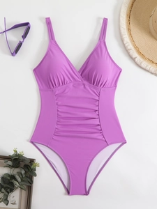 Flat lay of purple one-piece swimsuit with V-neckline, ruched details and vacation props