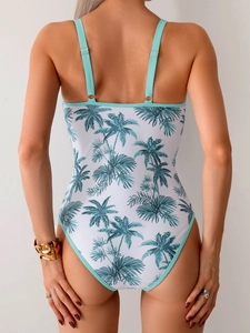 Detail of cross-back white swimsuit with teal palm leaf pattern and gold accessories