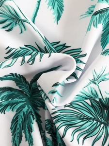 Close-up of tropical green palm leaf print on white elastic one-piece swimwear fabric