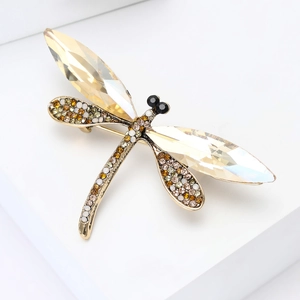 Detailed macro shot of a crystal dragonfly brooch with gold plating on a white stand