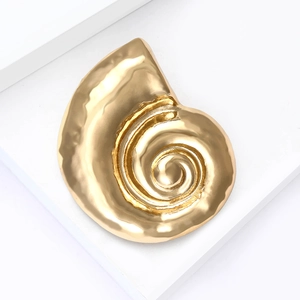 Close-up of golden snail shell brooch with metallic texture on white stone pedestal