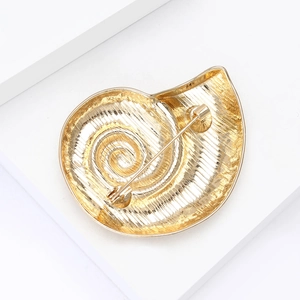 Macro shot of the backside of a golden snail shell brooch with a secure safety pin clasp