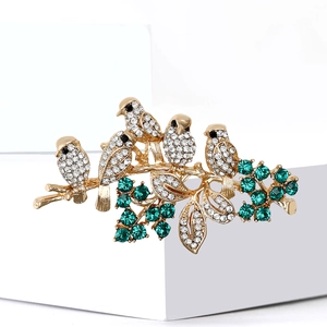 Exquisite gold bird brooch with white crystals and green gems on a branch