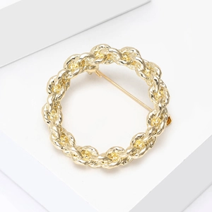 Macro view of a gold-toned circular brooch with elegant twisted rope texture design