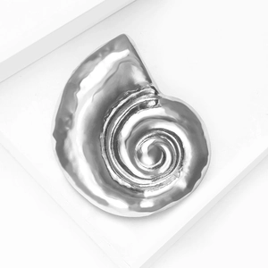 Macro shot of silver spiral snail shell brooch with polished mirror finish on white stairs