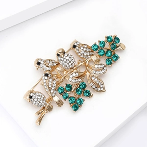 Detailed macro view of gold-tone bird brooch with emerald green crystals and clear rhinestones