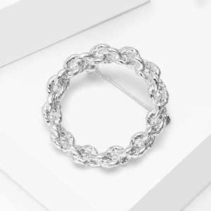 Detailed macro view of a silver circular twisted chain brooch on white platform
