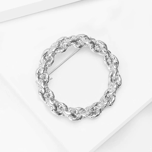 Detailed close-up of a silver-toned spiral twist brooch with metallic woven texture