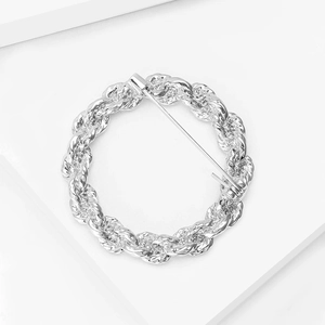 Detail view of silver round cable chain brooch with a pin clasp on a white platform