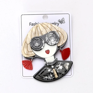 Broche chic en acrylique avec cheveux dorés et lunettes rouges sur carte de bijoux