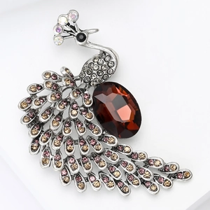 Détail d'une broche paon argentée avec une gemme rouge et des strass colorés brillants